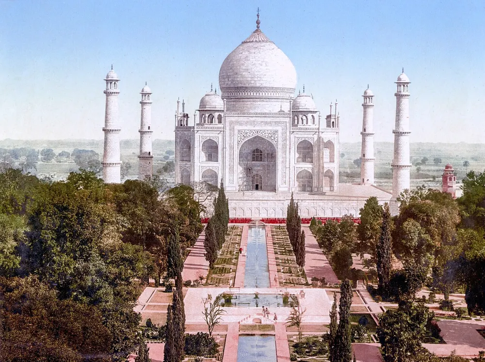 Vintage color print of a white marble domed tomb with four slender towers, seen beyond long garden pools